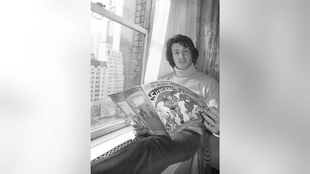 Sylvester Stallone reads a comic in a hotel room.
