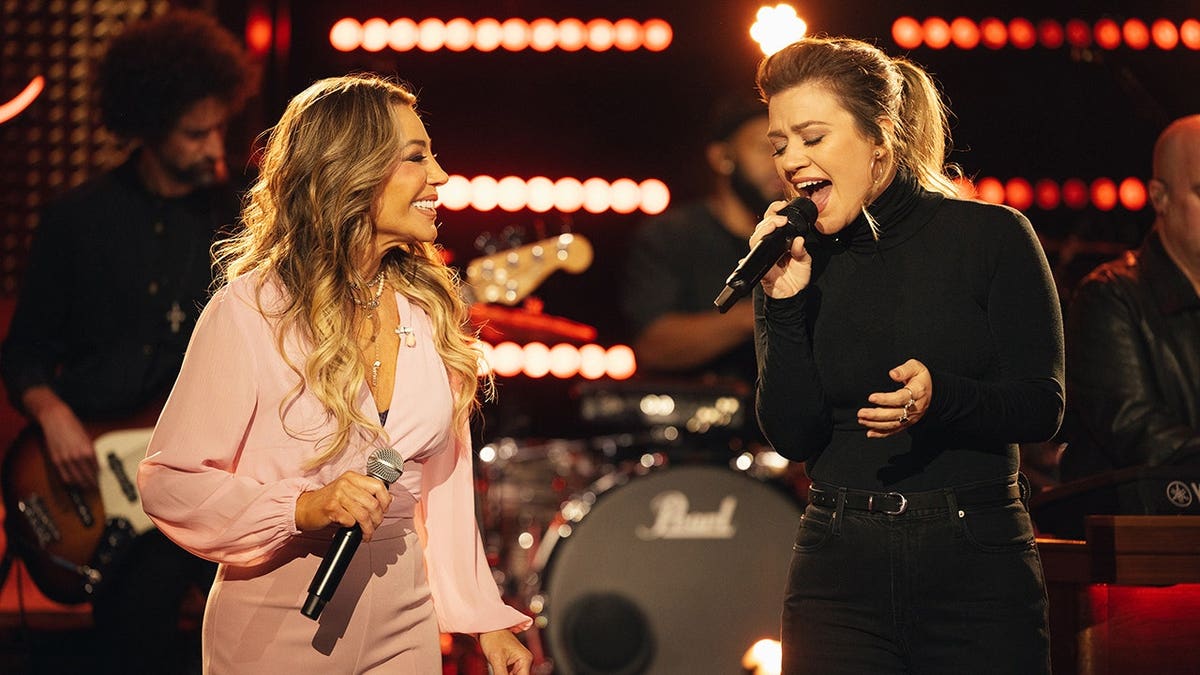 Taylor Dayne and Kelly Clarkson stand together on stage.