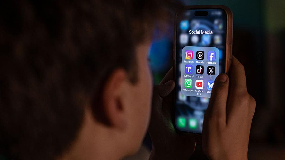 A 13-year-old boy looks at an iPhone screen displaying social media apps.