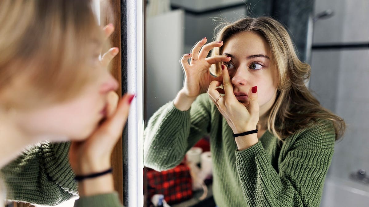 Teenage girl inserts a contact lens in a bathroom.