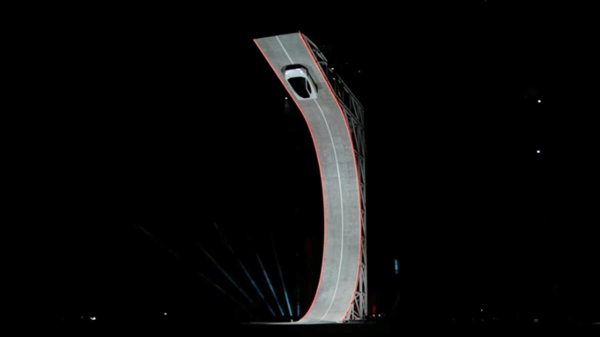 The Tesla Roadster climbs a curved ramp, nearly upside-down.