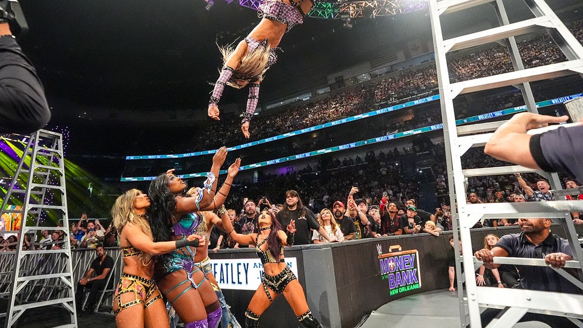 Tiffany Stratton dives off a ladder onto four wrestlers in the ring.