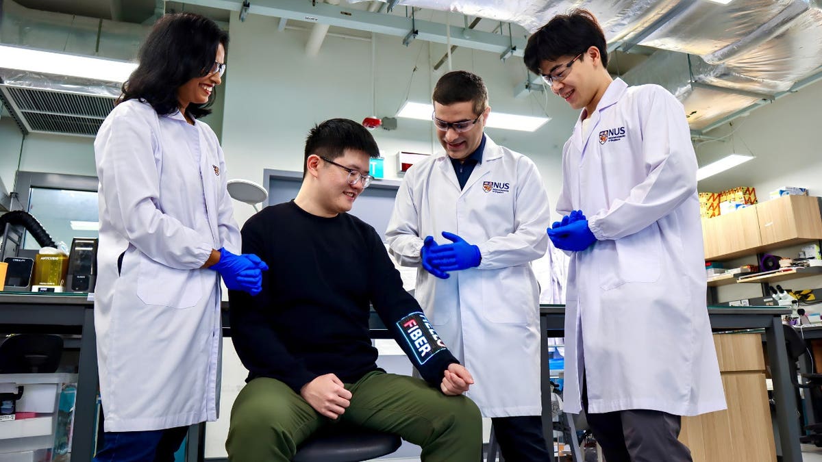 A team of scientists surrounds a person wearing a shirt with a digital sleeve.
