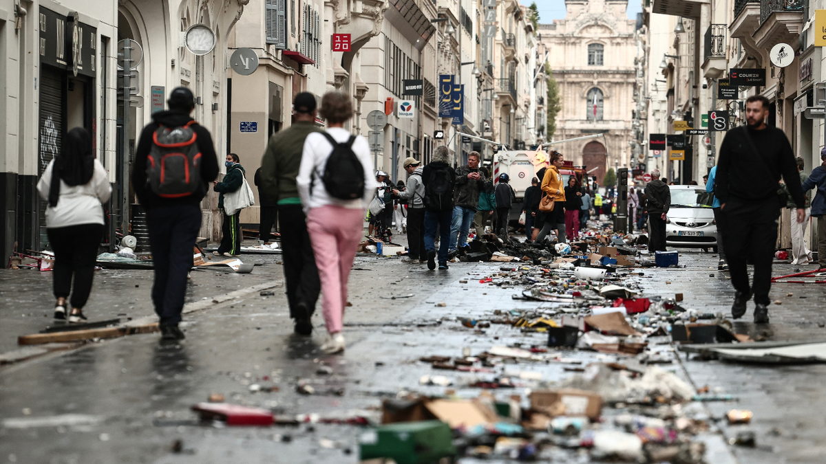 Pedestrians walk along a street covered in debris a day after nationwide protests against the 
