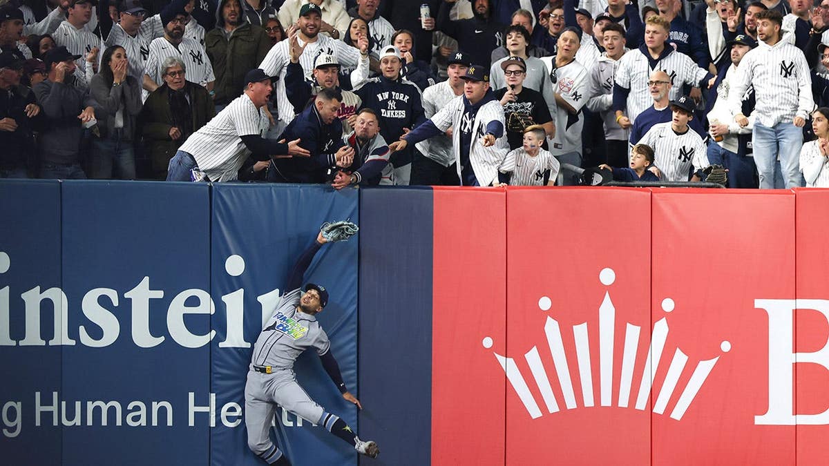 Victor Mesa Jr. of the Tampa Bay Rays reaches for a ball as fans interfere at Yankee Stadium.