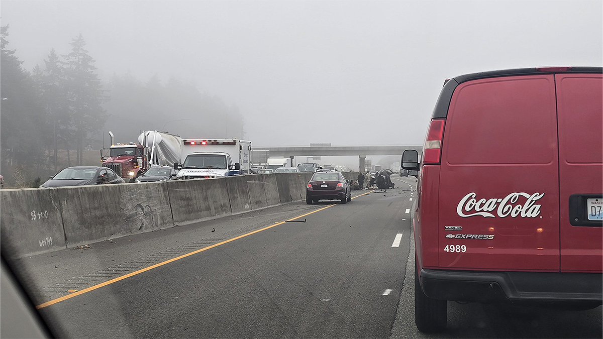 Bystanders, including people in military uniforms, gather beside an overturned SUV on I-5 near DuPont, Washington