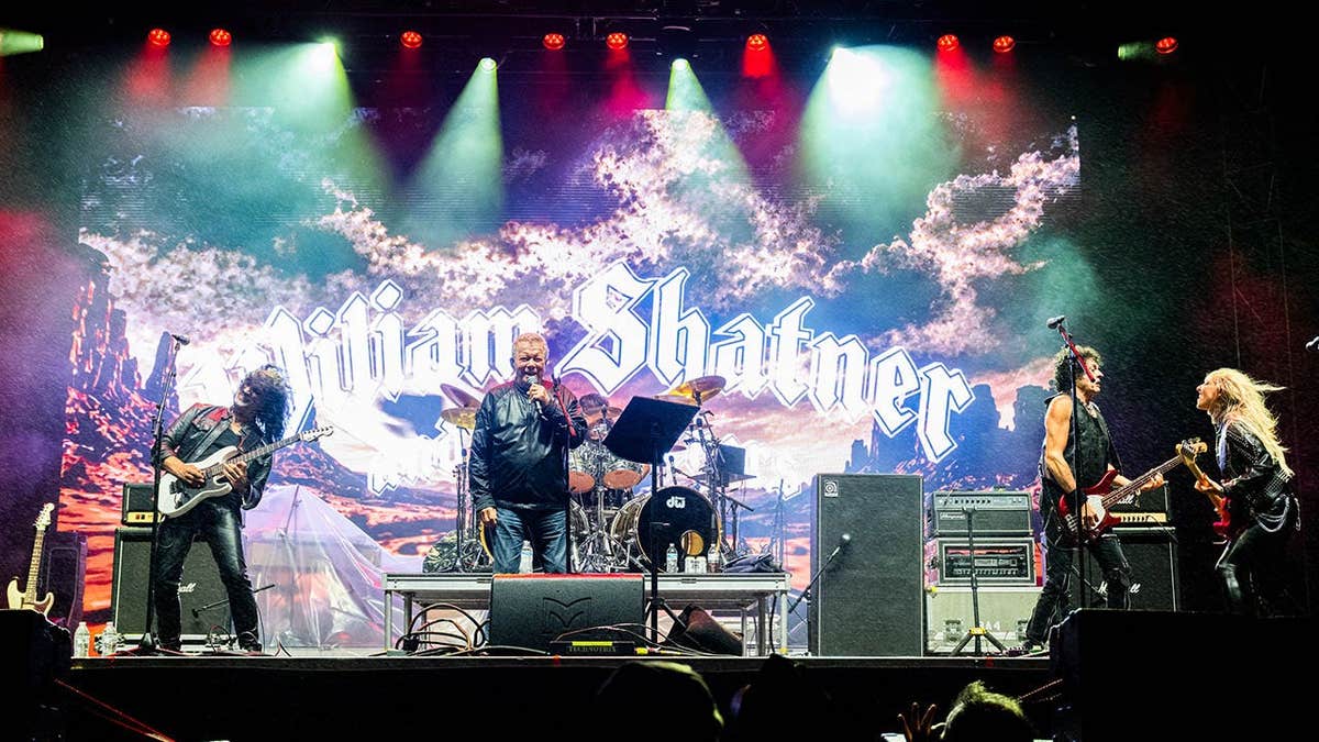 William Shatner performs on stage with band members Marcus Nand, Phil Soussan and Britt Lightning.