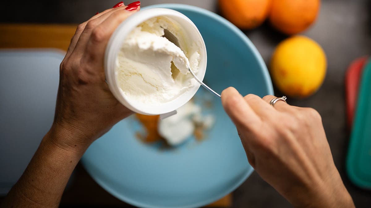 Woman spoons fresh ricotta into a blue mixing bowl for baking.