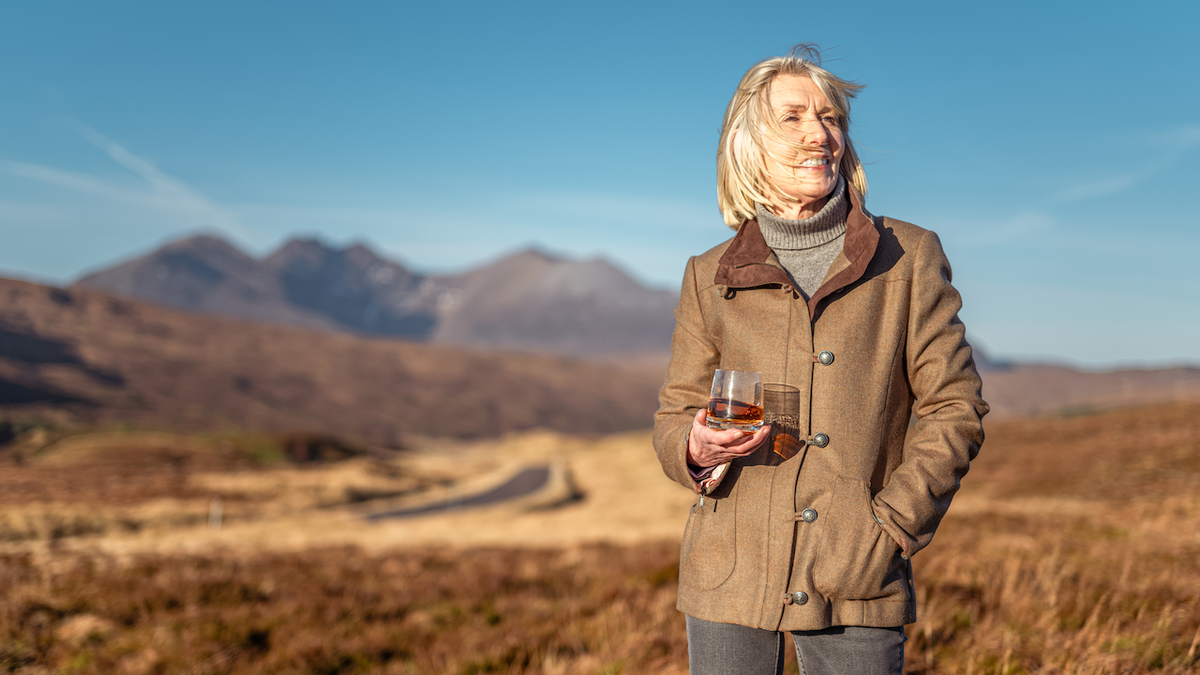 Woman relaxing with a dram of whisky in a mountain landscape in Scotland.