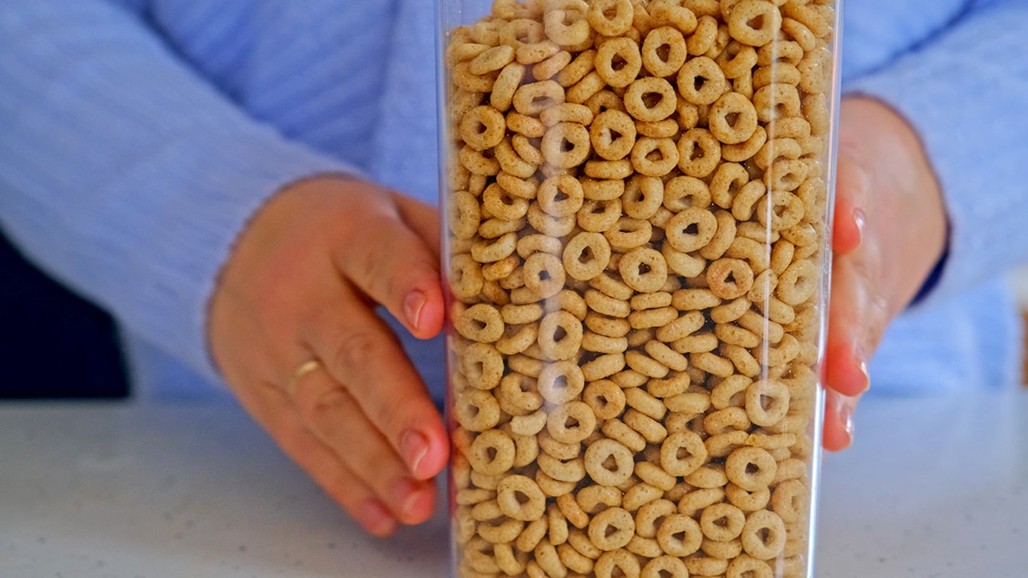 A woman's hands touch a cereal container filled with Cheerios.