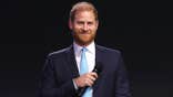 Prince Harry smiling in a suit onstage.