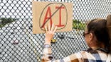 Person holds up sign on pedestrian bridge during anti-AI protest in Berkeley.