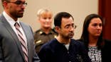 Larry Nassar stands with defense attorneys Matt Newberg and Molly Blythe in a courtroom.