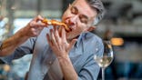 A man eats pizza and appears to enjoy it inside a pizzeria.