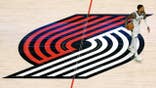 Damian Lillard dribbles the ball on the Portland Trail Blazers center court logo during an NBA game.