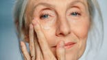 Senior woman applying under-eye face cream to her face.