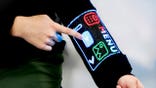 A person touches a digital display on the sleeve of a shirt.