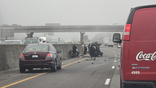 People in military uniforms and other bystanders assist beside an overturned SUV with debris scattered across I-5
