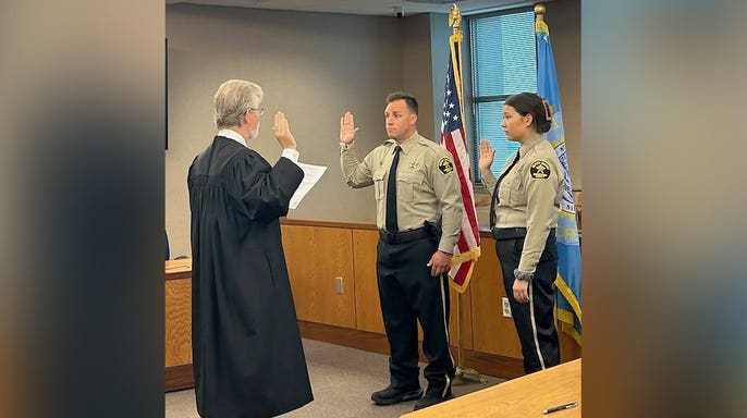 A judge in a black robe administers the oath of office to two Minnehaha County sheriff's deputies, including Katherine Frank, standing with their right hands raised.