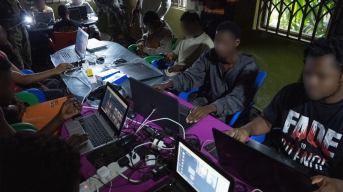 People seated at tables using laptop computers inside a suspected scam center in Ghana