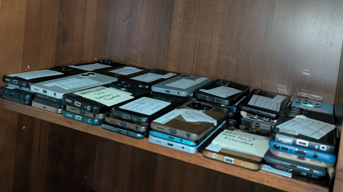 Dozens of labeled smartphones arranged on a wooden shelf during a scam center investigation in Ghana