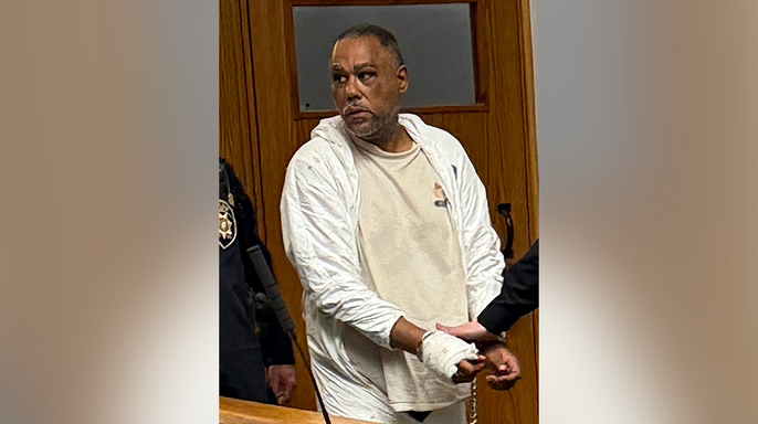 Nelson Blanco stands in court wearing white protective clothing with a bandaged hand