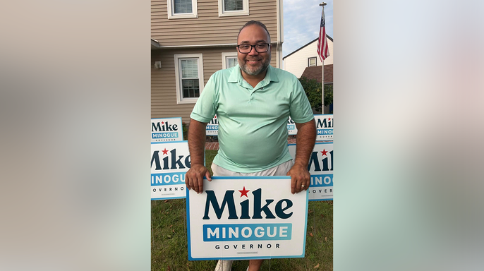 Shawn Oliver holds a Mike Minogue for governor sign outside a home