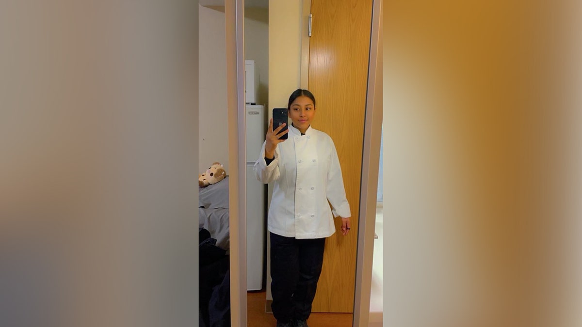 Angelina Resendiz takes a mirror selfie while wearing a white culinary uniform inside her barracks room.